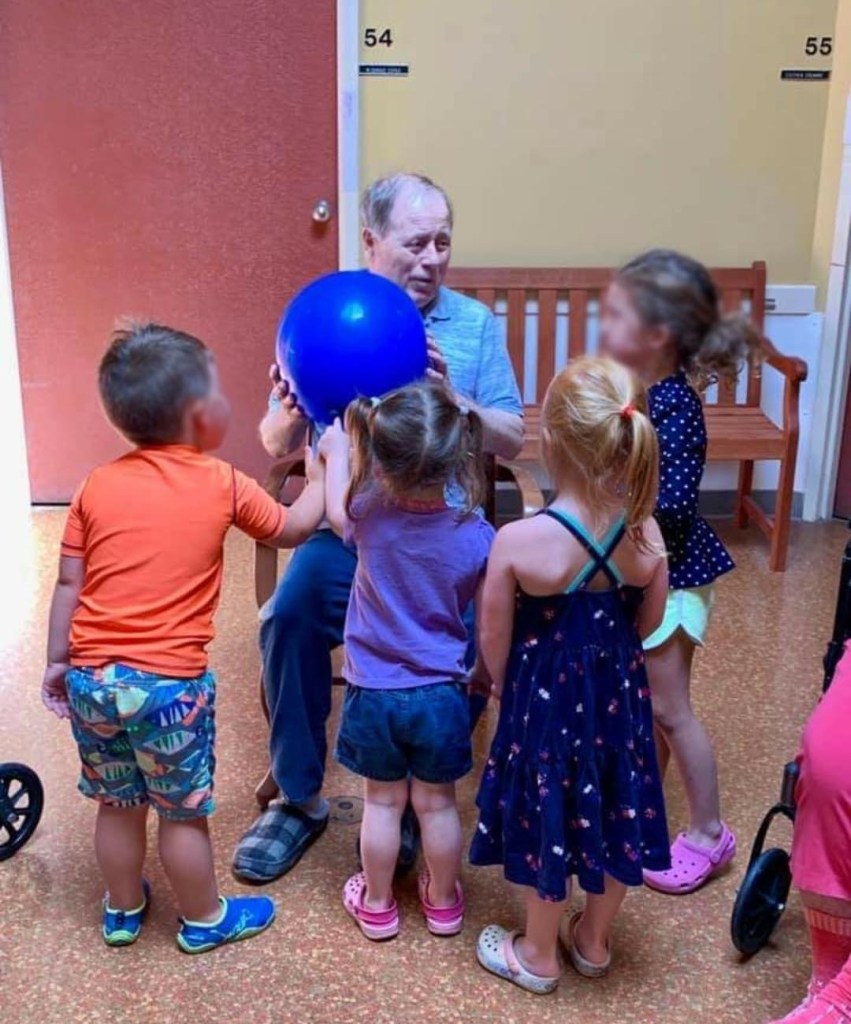 Photo of Russ holding a large ball and surrounded by young children.